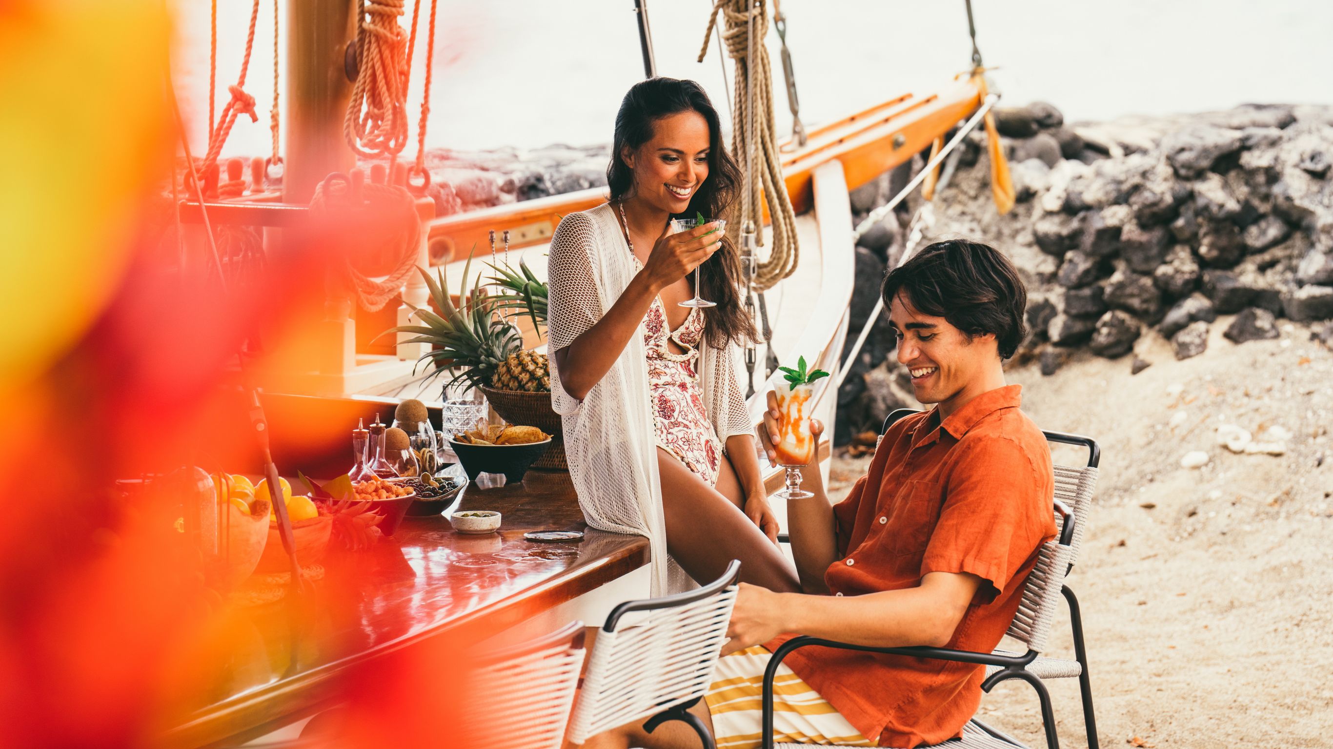 A couple enjoying drinks at a beach bar with  a boat in the background.